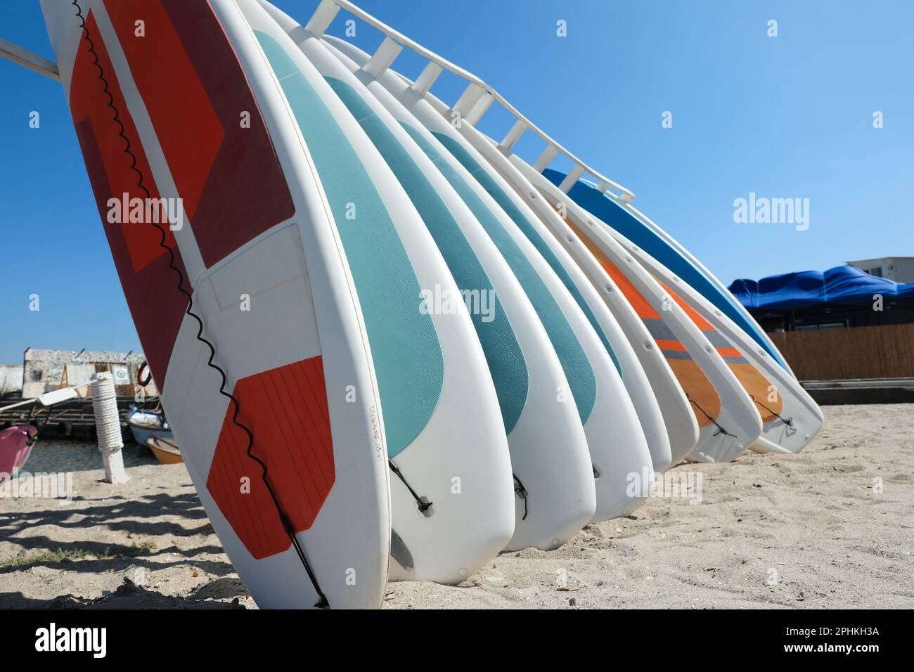 Rack avec planches de paddle colorées sur le sable près de la mer Banque D'Images Rack avec planches de paddle colorées sur le sable près de la mer Banque D'Images