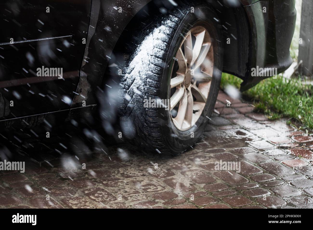 roue de voiture dans les pneus d'hiver par mauvais temps avec de la neige quand l'herbe devient verte. Phénomènes naturels anormaux Banque D'Images