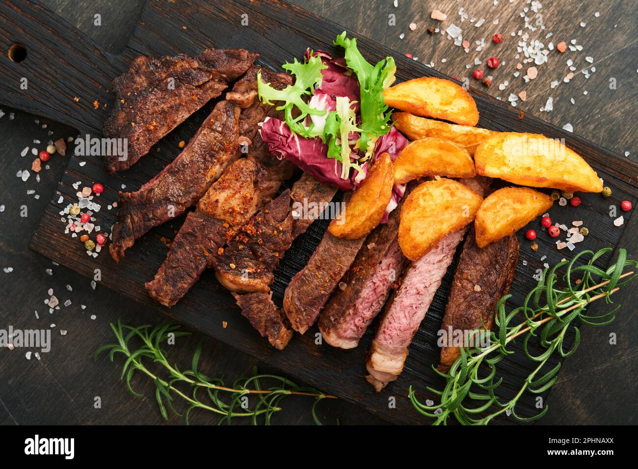 Steaks. Steak de viande grillée en tranches New York, Ribeye ou Chuck rouler avec garniture de salade et frites sur un plateau en marbre noir sur le vieux b bois Banque D'Images