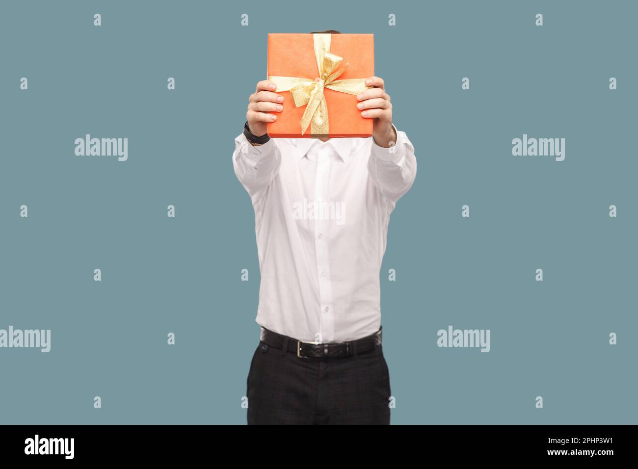 Portrait d'un homme anonyme inconnu tenant et couvrant son visage avec une  boîte cadeau rouge, donnant le cadeau pour anniversaire, en portant un  studio d'intérieur tourné isolé sur fond bleu clair Photo