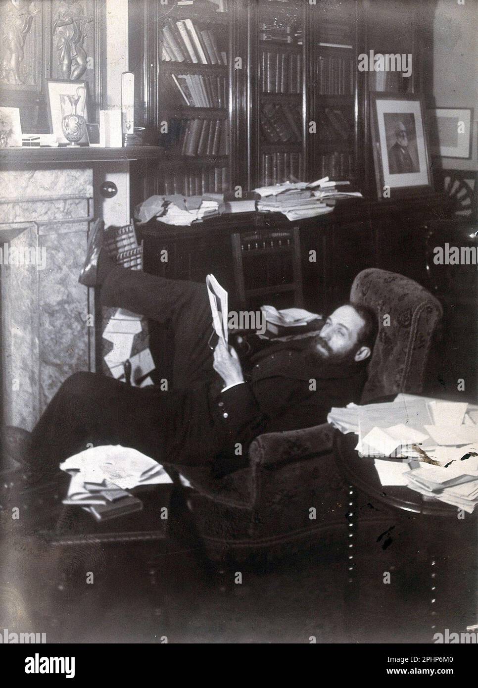 Arthur Schuster, physicien britannique d'origine allemande allongé sur un fauteuil près d'une cheminée, avec une photo de Lord kelvin derrière lui, photographie d'époque de c1901 Banque D'Images