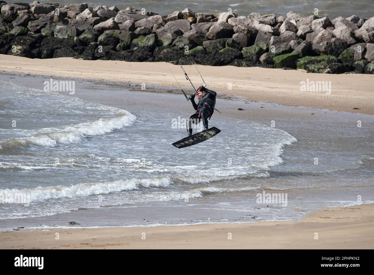 Un Kitesurfer avec harnais, barre de commande et lignes devient aéroporté quand de forts vents lèvent sa canopée de la rive ouest à Llandudno par temps venteux Banque D'Images