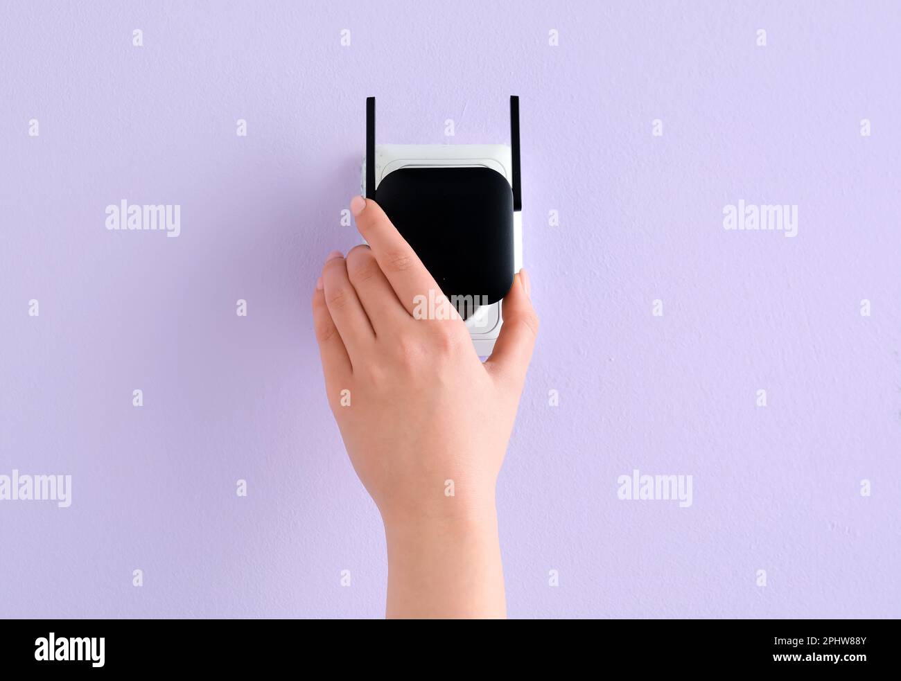 Femme branchant un répéteur WiFi noir dans une prise électrique murale lilas Banque D'Images