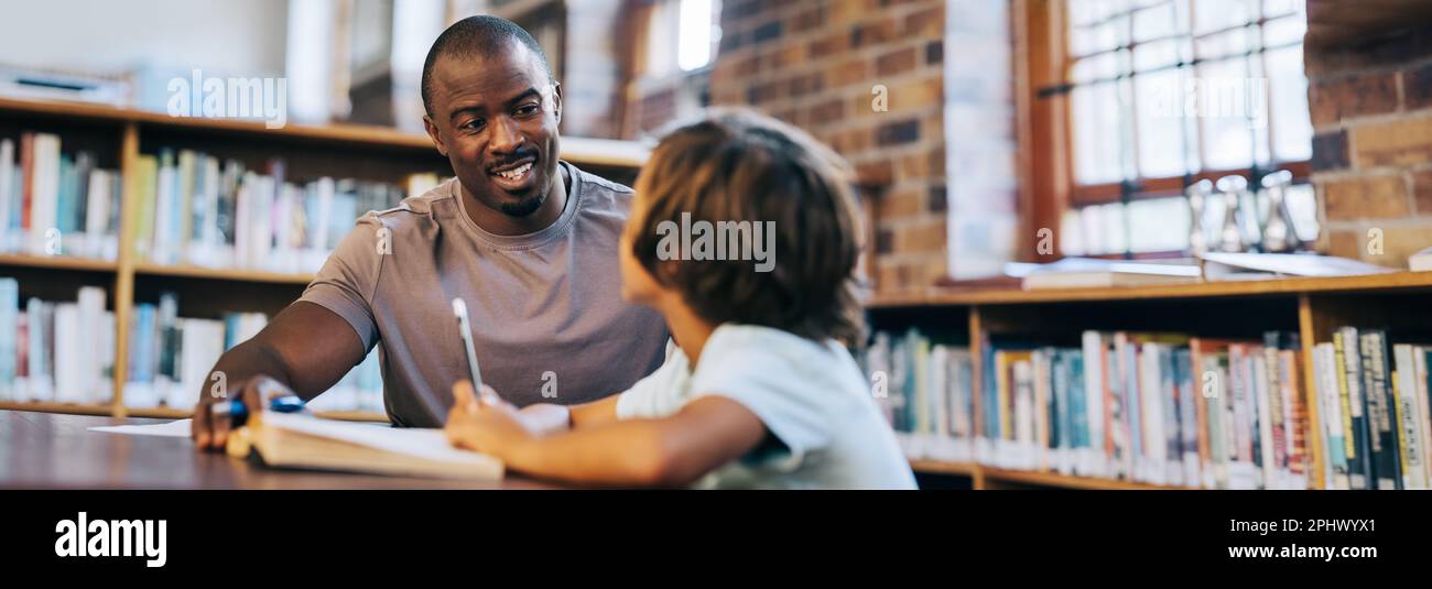 Un enseignant de sexe masculin conseille un jeune garçon d'école dans une bibliothèque. Professeur d'école primaire parlant à un étudiant dans une session privée. Thérapie et souper pour enfants Banque D'Images