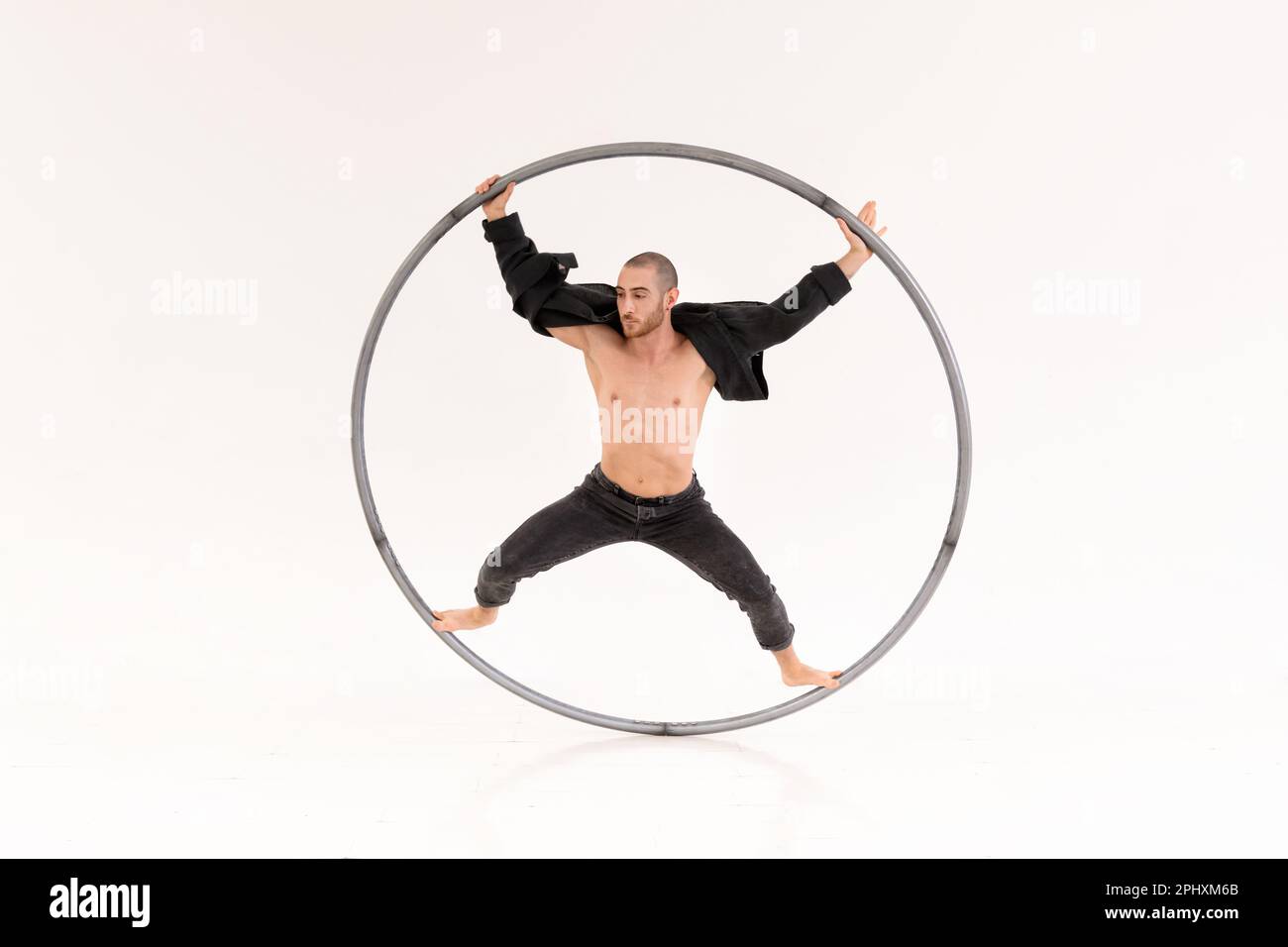 Corps complet de l'artiste cyr Wheel masculin concentré en train de jouer le tour dans la pièce blanche Banque D'Images