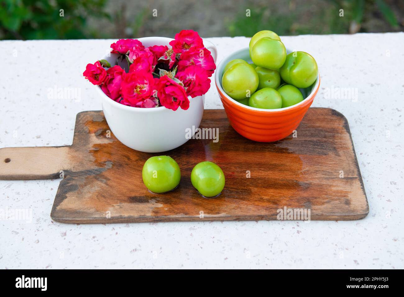 Disposition avec des bols avec roses roses roses et prunes vertes à l'extérieur en été. Banque D'Images