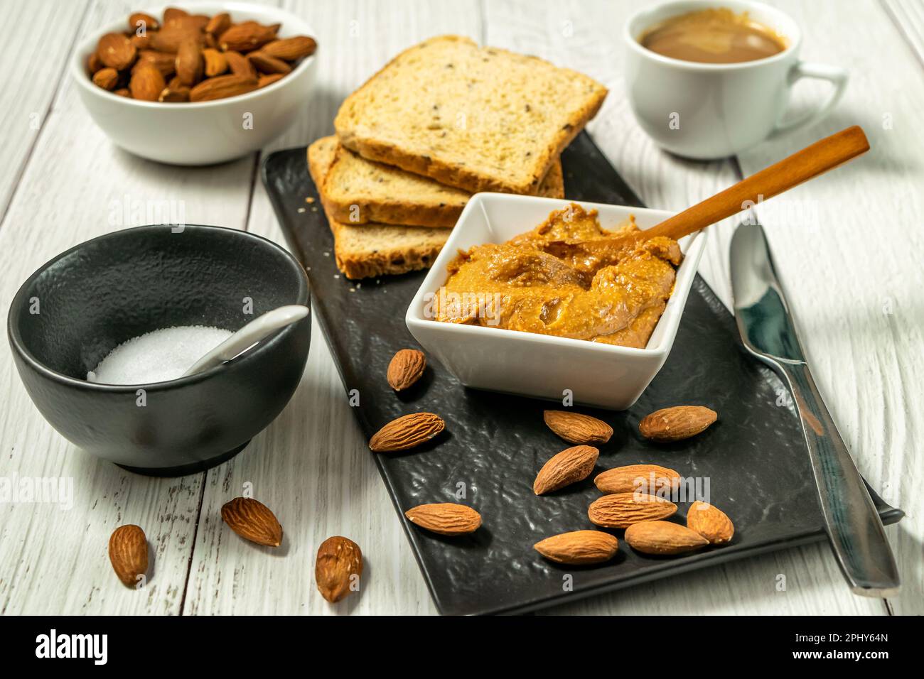 Dans un bol sur la table, le beurre d'amande biologique cru avec une cuillère en bois et des amandes éparpillées sur la table, griller le pain et le café Banque D'Images
