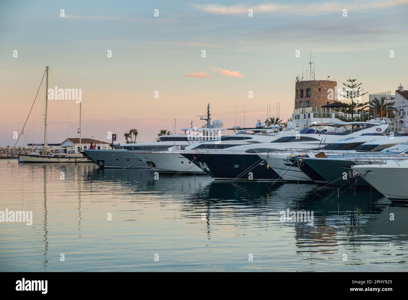 Yachts de luxe à la lumière de la soirée amarré à Puerto Banus Marina, Marbella, Espagne avec la tour de contrôle maritime en arrière-plan Banque D'Images