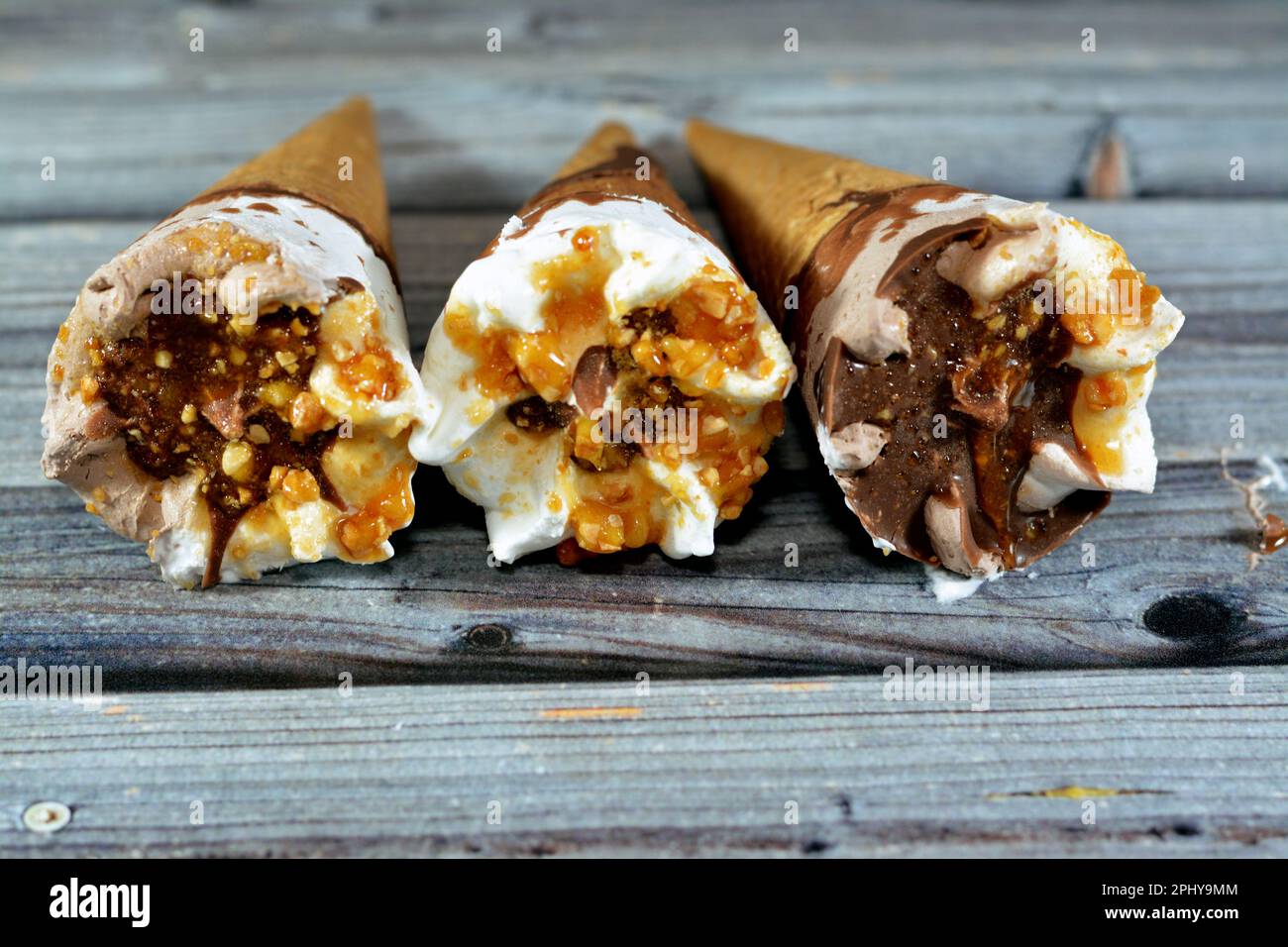 Cornets de vanille et de chocolat à la crème glacée avec garniture de chocolat et de sauce caramel et noix dans des cornets croustillants, fondant la crème glacée froide dans un tourbillon Banque D'Images