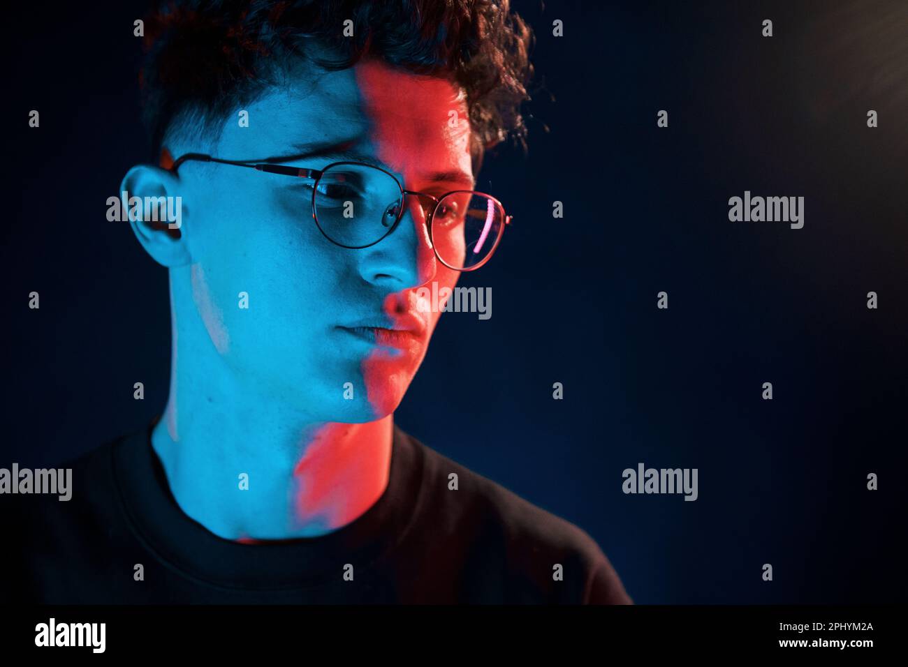 Sur fond noir. Éclairage au néon. Le jeune homme européen est dans le studio sombre Banque D'Images