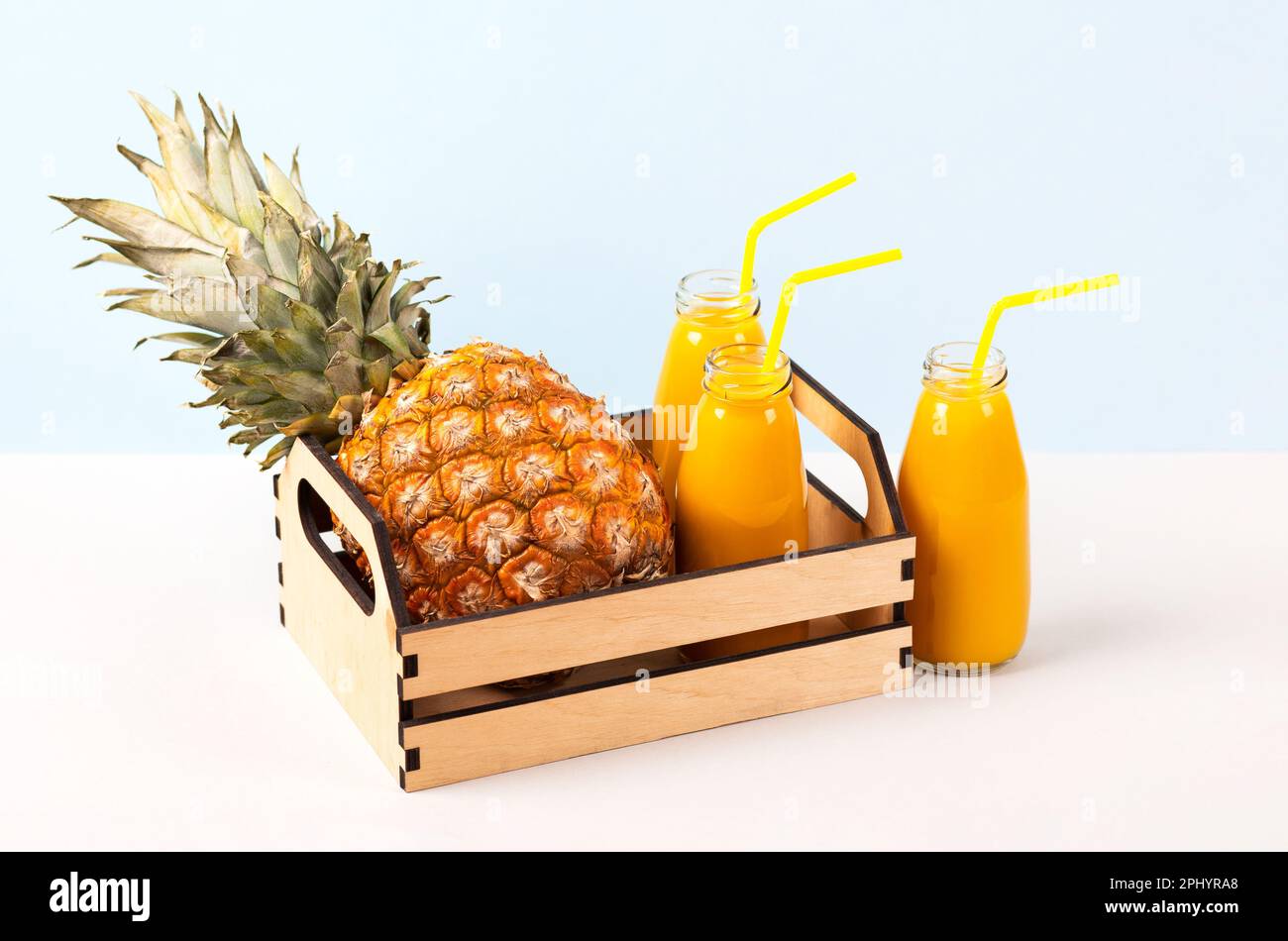 Ananas dans une boîte en bois et un smoothie frais et sain dans des bouteilles de verre et une paille sur fond bleu. Santé, désintoxication et alimentation conce Banque D'Images