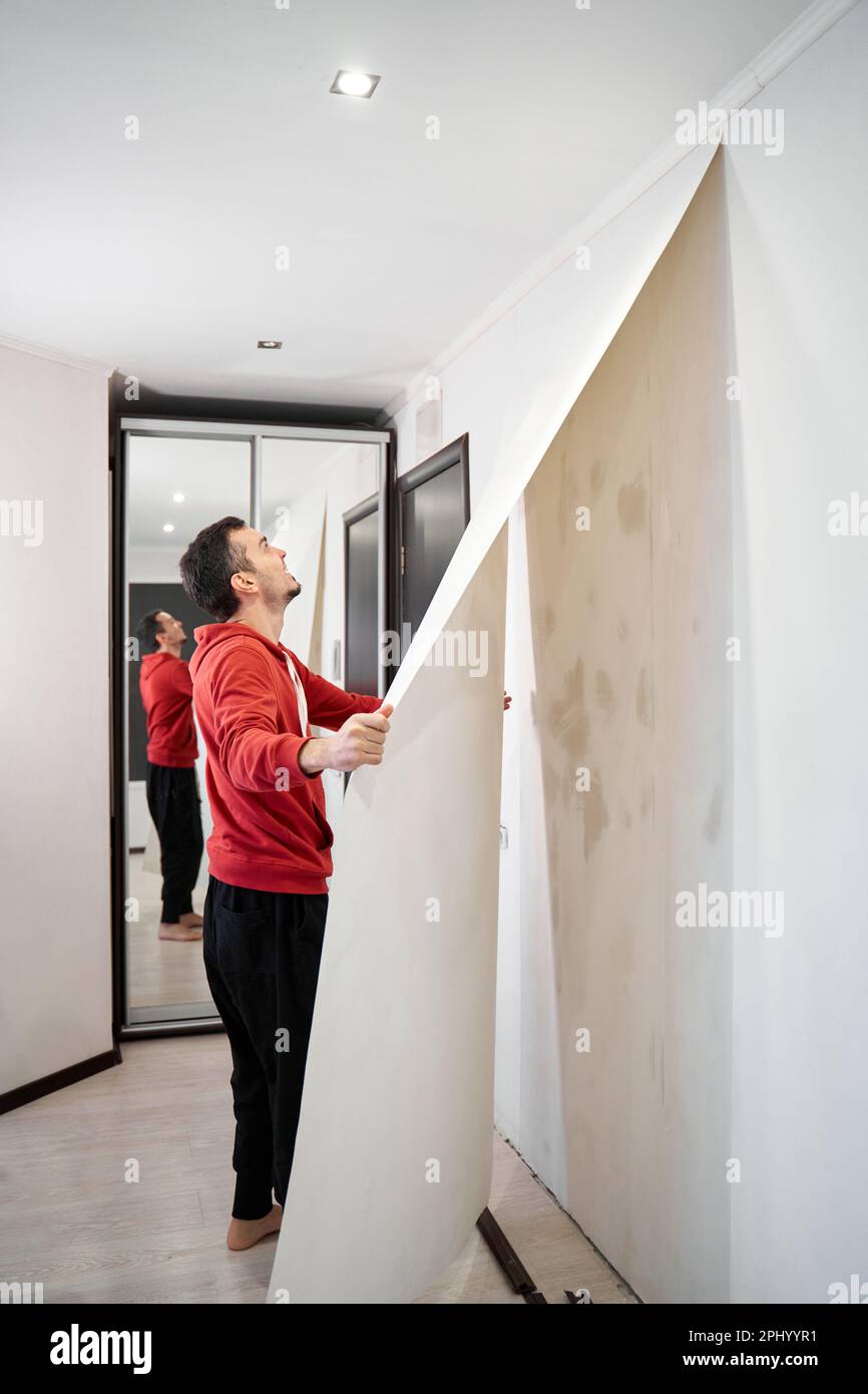 Réparer la maison avec leurs propres mains. Le gars arrache le vieux papier  peint du mur Photo Stock - Alamy
