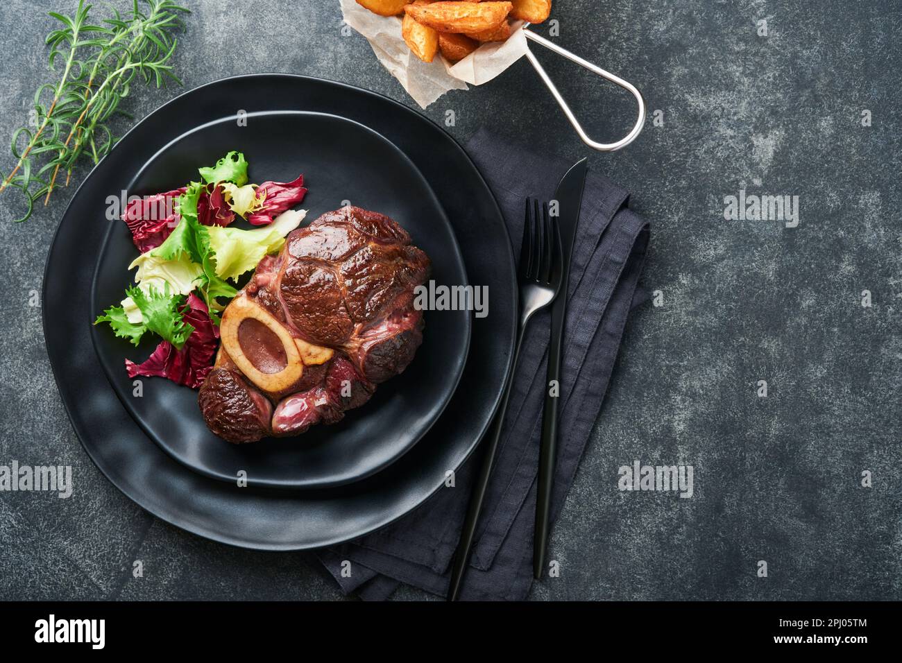 Steaks Osso Buco. Bœuf grillé Osso Buco ou steak de viande de portreuse avec garniture de salade et de frites sur un panneau de marbre noir sur du vieux bois Banque D'Images