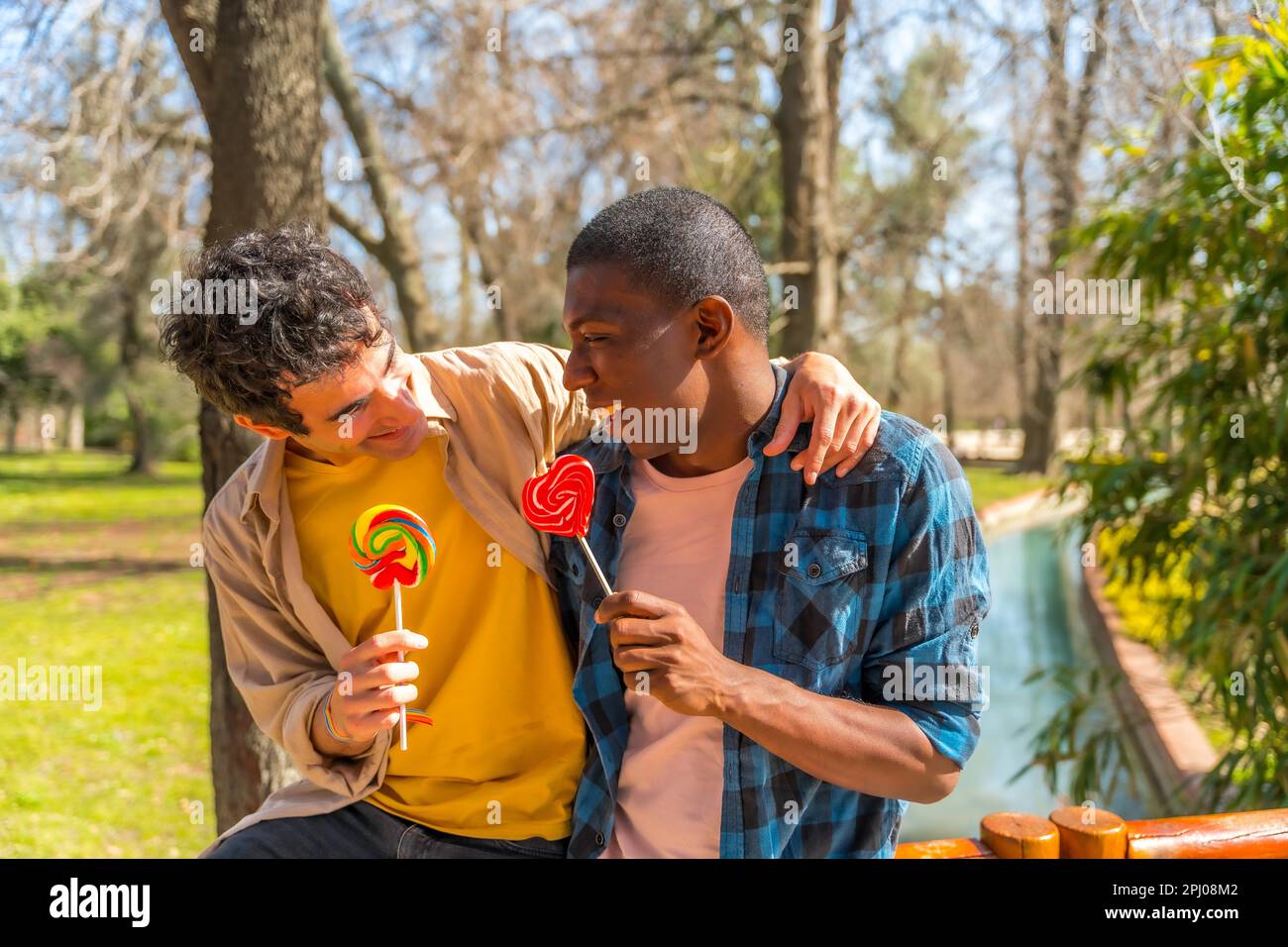 Couple d'hommes multiethniques mangeant un lollipop, lgbt concept, ayant le plaisir et sourire dans un parc Banque D'Images