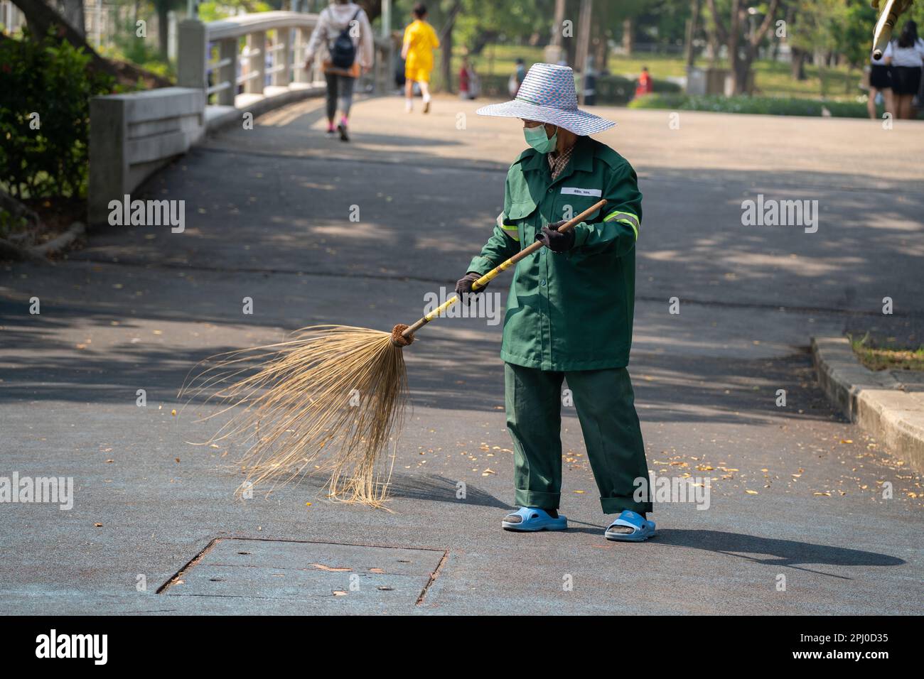 Lady Street Cleaner dur au travail dans le parc Lumphini, Bangkok en utilisant un balai et une brouette comme elle fait son chemin à travers le parc. Banque D'Images