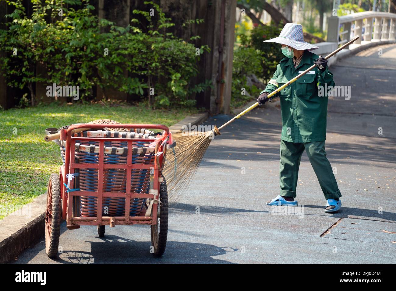 Lady Street Cleaner dur au travail dans le parc Lumphini, Bangkok en utilisant un balai et une brouette comme elle fait son chemin à travers le parc. Banque D'Images