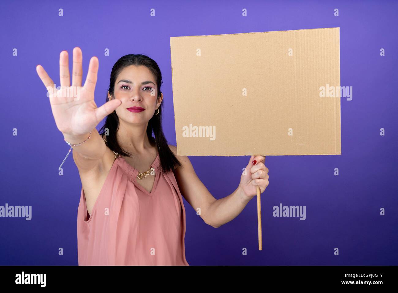 jeune femme tenant une pancarte dans une main et faisant un panneau stop sur un fond violet isolé Banque D'Images