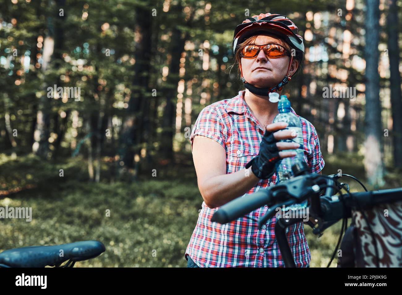 Femme active qui passe des vacances d'été gratuites lors d'un voyage à vélo dans une forêt. Femme portant un casque de vélo et des gants tenant un vélo avec un panier et un dr Banque D'Images