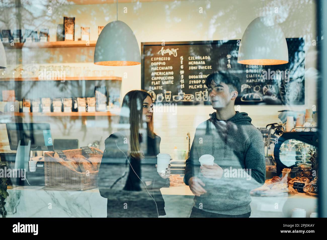 Amis qui ont une discussion, tenant des tasses de café, debout dans un café et attendant leurs commandes. Homme et femme ayant une pause boire du café moi Banque D'Images