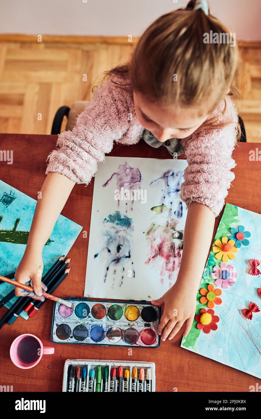 Petite fille de pré-chooler peignant une image en utilisant des peintures colorées et des crayons. Enfant s'amusant à prendre une photo pendant un cours d'art en classe Banque D'Images