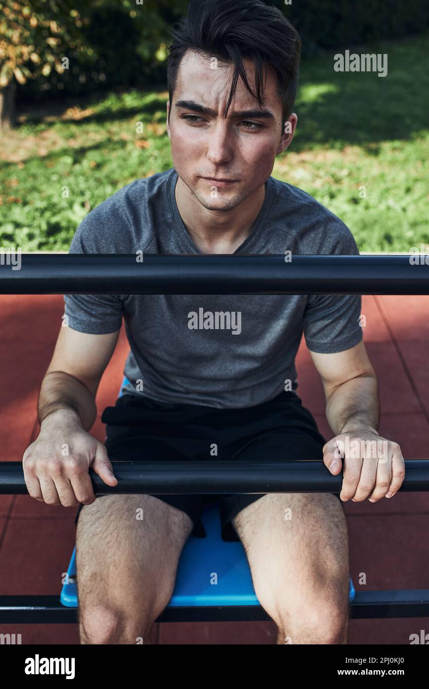 Portrait d'un jeune homme ayant une pause pendant son entraînement dans un parc d'entraînement moderne de rue calisthénique. Homme assis sur une planche assise portant des vêtements de sport l Banque D'Images