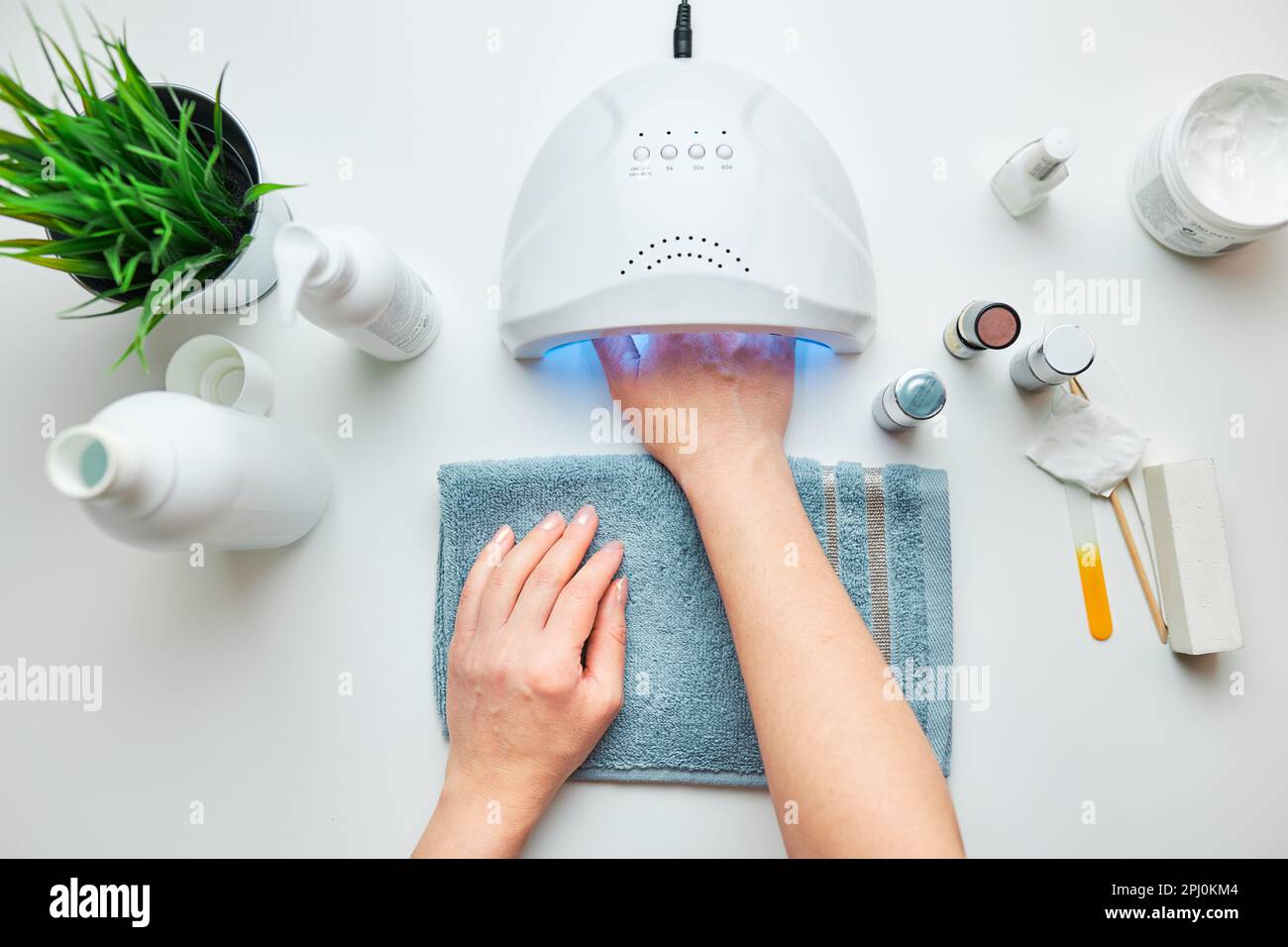 Femme appliquant du gel hybride à l'aide d'une lampe UV. Beauté bien-être concept de soins spa. Produits cosmétiques, lampe UV, feuilles vertes sur table blanche. Spa, m Banque D'Images