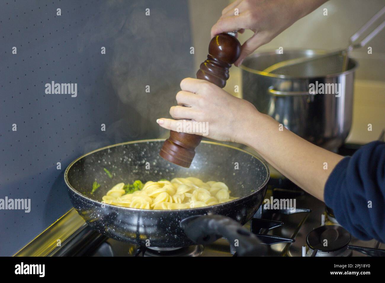 Image des mains d'une femme assaisonnant des pâtes fraîchement cuites dans une casserole avec un moulin à poivre. Tradition culinaire italienne. Banque D'Images