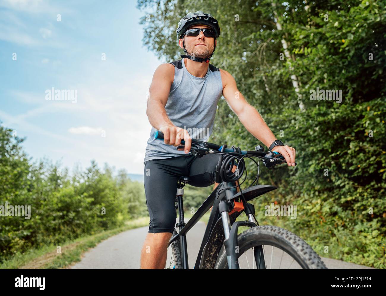 Portrait d'un heureux homme vêtu de vêtements de cyclisme, d'un casque et de lunettes de soleil sur un vélo sur la piste cyclable de l'extérieur de la ville. Concept sportif actif Banque D'Images