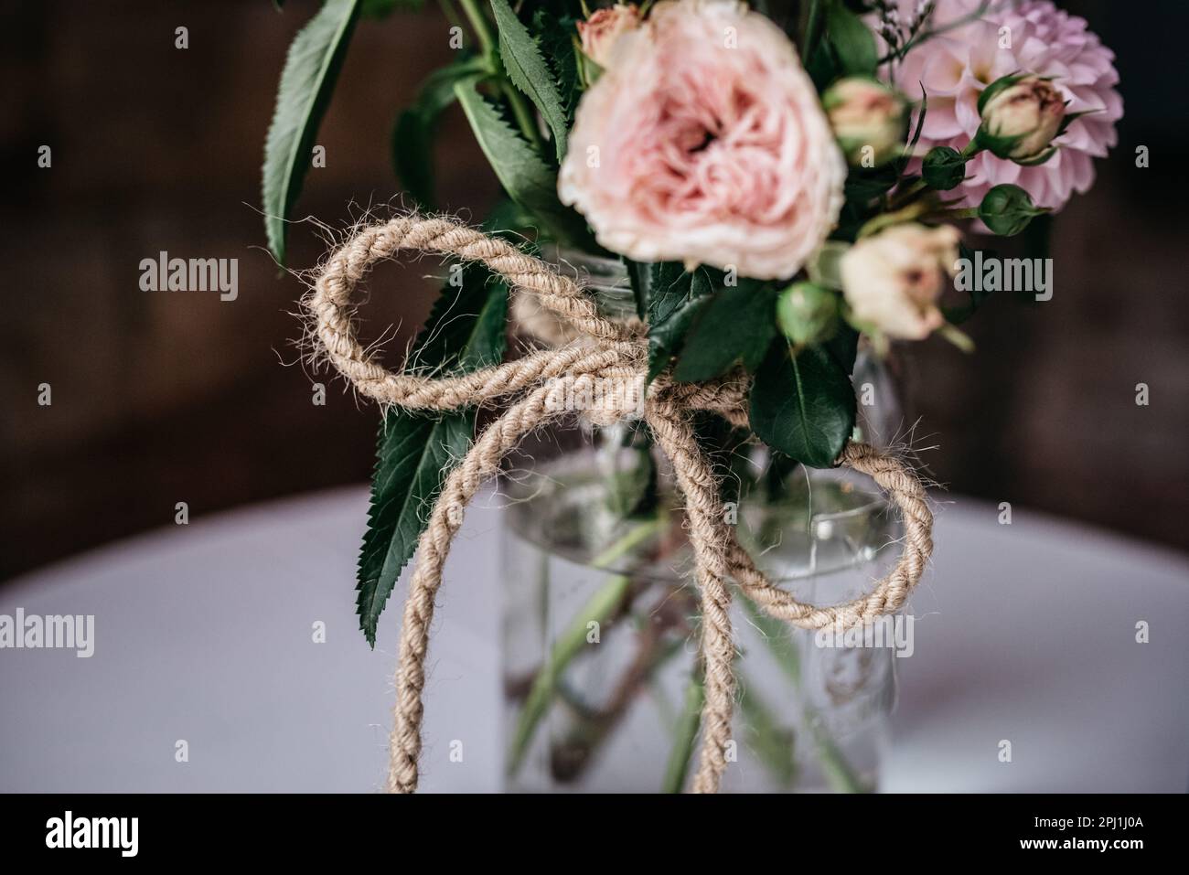 Un arrangement de fleurs vibrantes dans un petit vase en verre, orné de ficelle de jute, ce qui fait un bel étalage Banque D'Images
