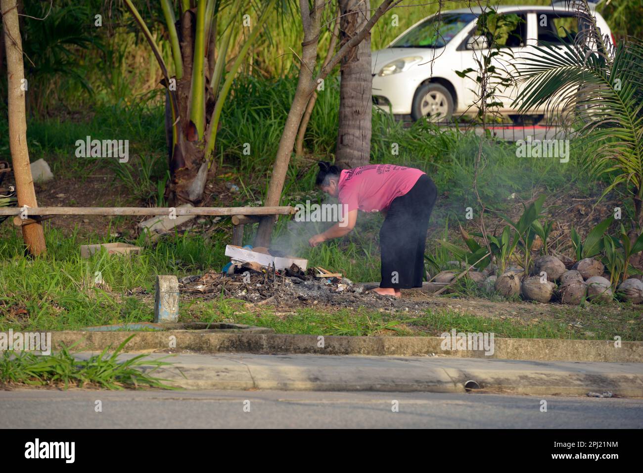 Une femme brûlant des ordures près de la plage à la pointe de Bornéo, Malaisie. Banque D'Images