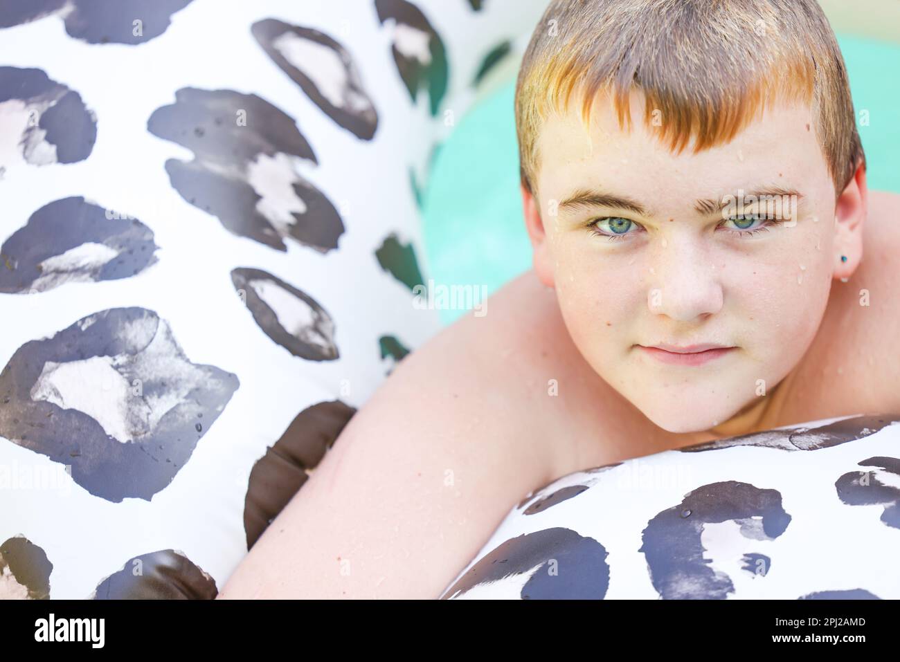 Gros plan d'un garçon d'avant-adolescence flottant sur un anneau gonflable à imprimé léopard Banque D'Images