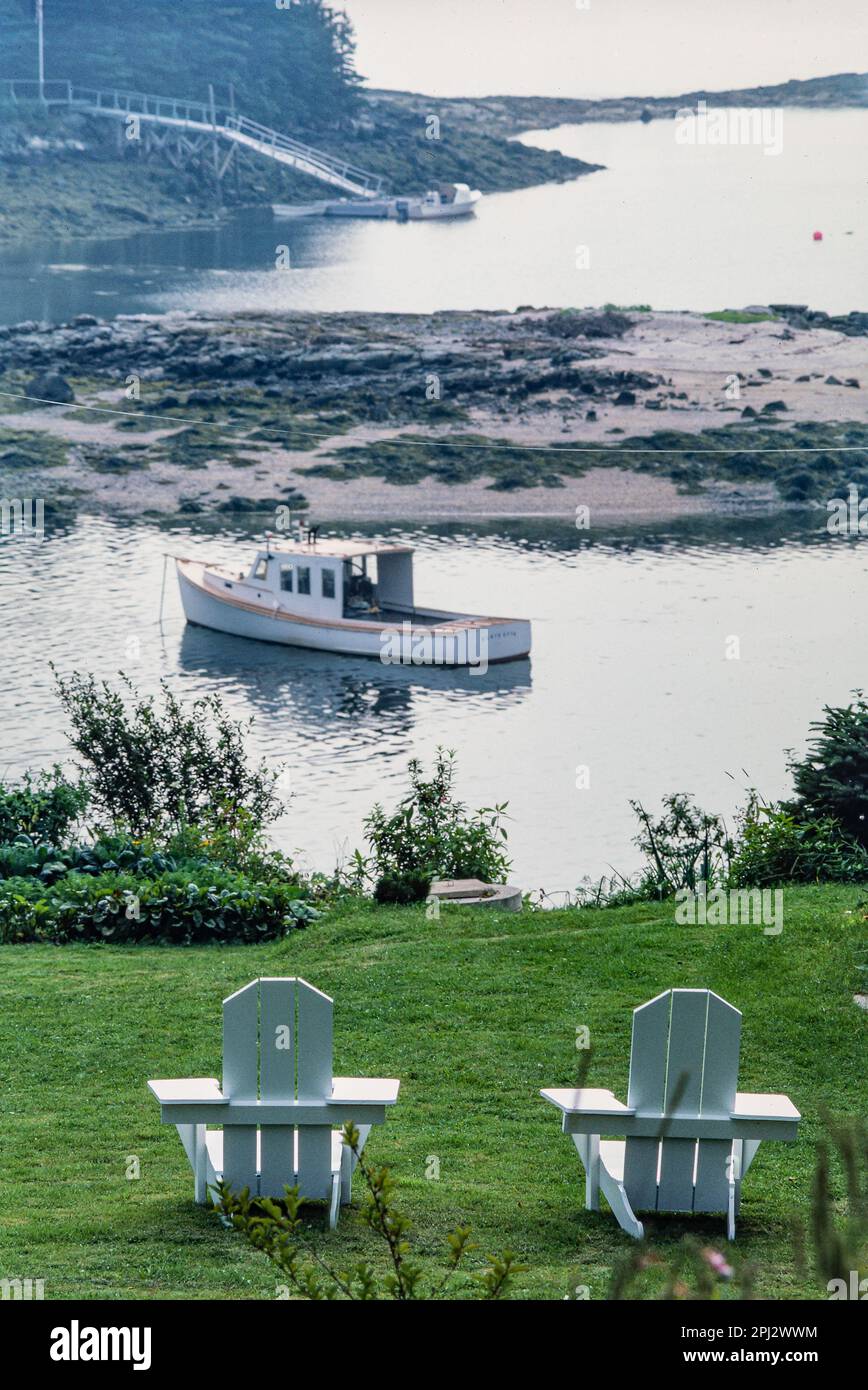 Les chaises blanches adirondack donnent sur une petite baie avec un bateau  de pêche de style downeast attaché et une sortie vers l'océan Atlantique à  Port Clyde, Maine Photo Stock - Alamy