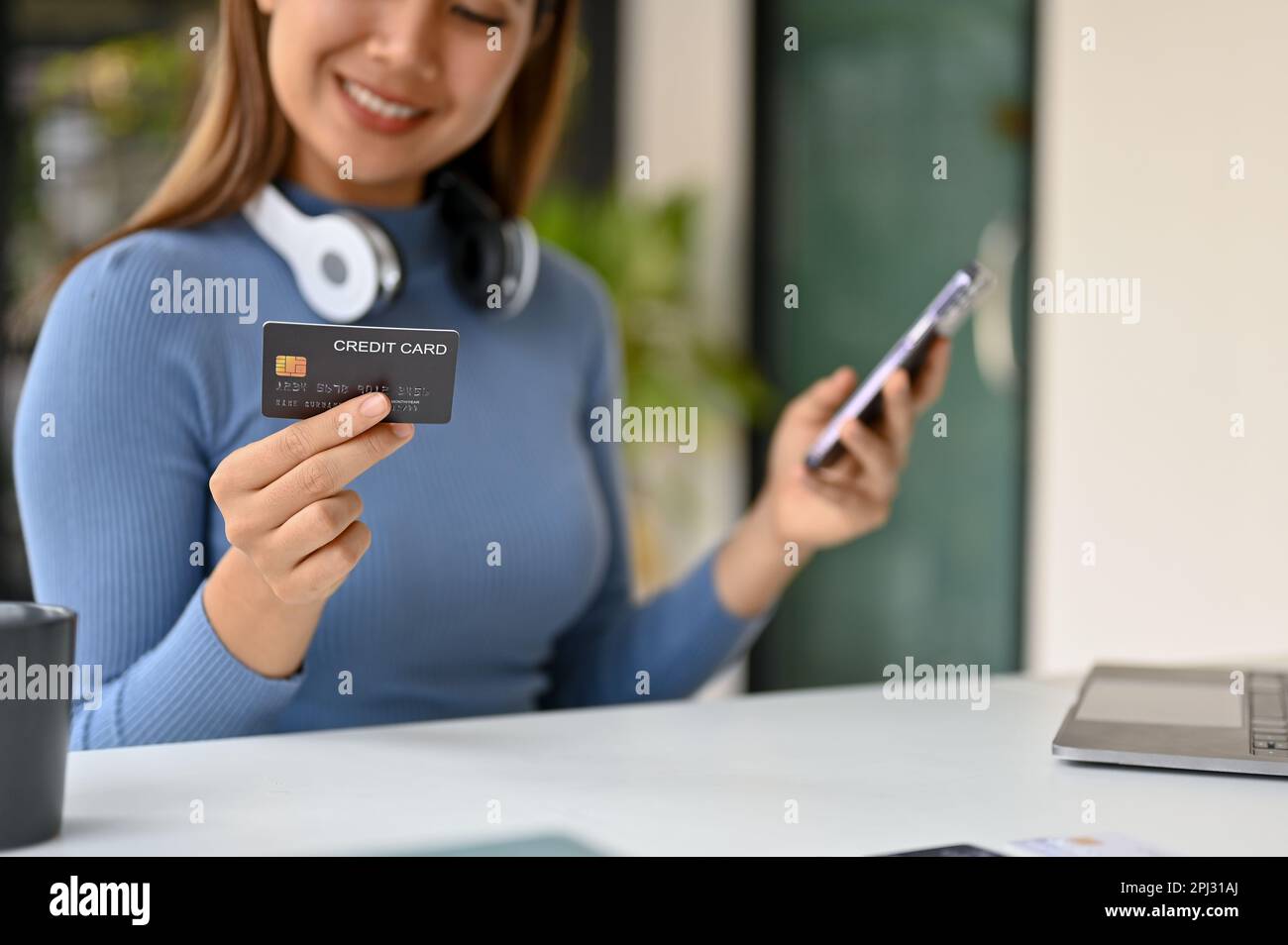Une image rapprochée d'une femme asiatique millénaire souriante se trouve à une table, tient sa carte de crédit et son smartphone, et utilise l'application bancaire mobile pour payer les données en ligne Banque D'Images