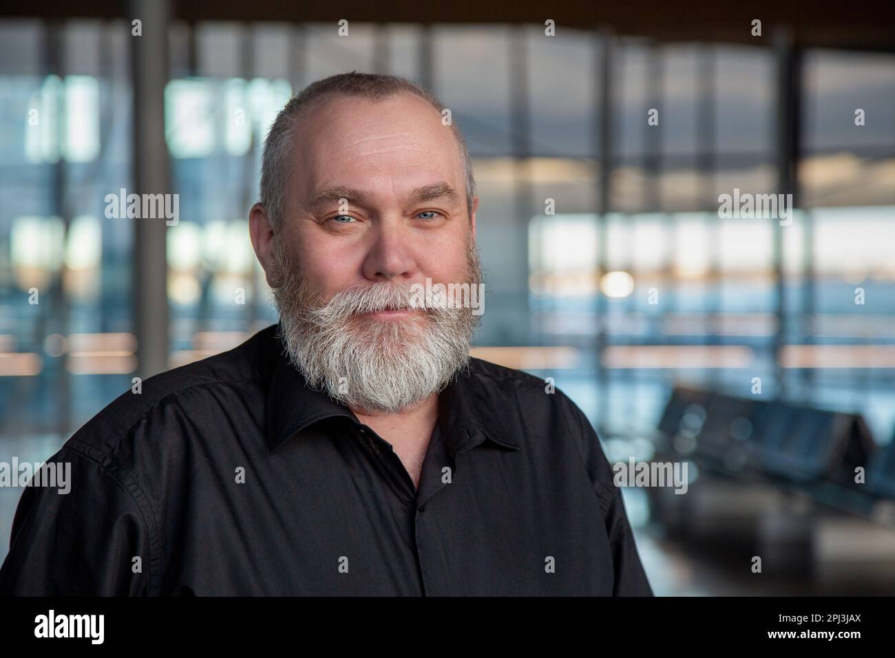 Portrait d'un homme d'âge moyen barbu. Joyeux homme âgé de 50 55 60 ans avec une barbe grise à l'aéroport, au bureau, à l'intérieur, en arrière-plan regardant la caméra Banque D'Images