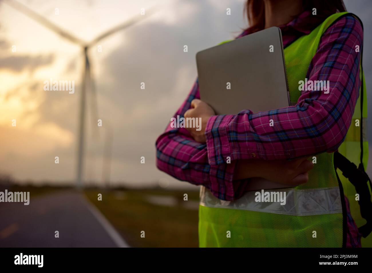 Femme asiatique travaillant avec un ordinateur portable dans une exploitation d'énergie renouvelable. Inspecteur féminin contrôlant le fonctionnement des éoliennes à l'extérieur. Banque D'Images