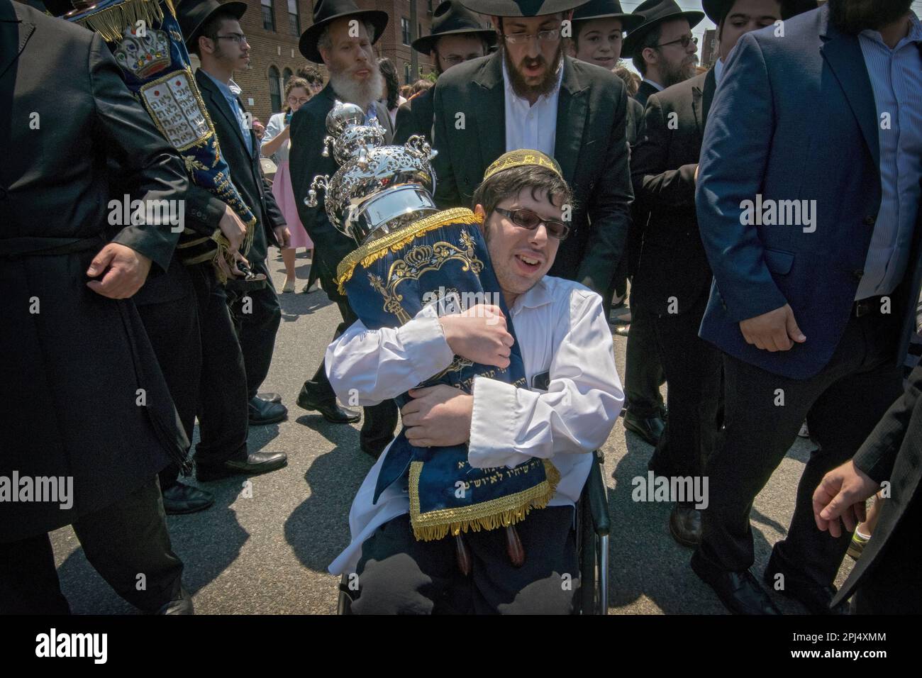 Lors d'une célébration de l'écriture d'une nouvelle Torah, un jeune juif en fauteuil roulant embrasse le défilement avec passion. À Far Rockaway, Queens, New York. Banque D'Images