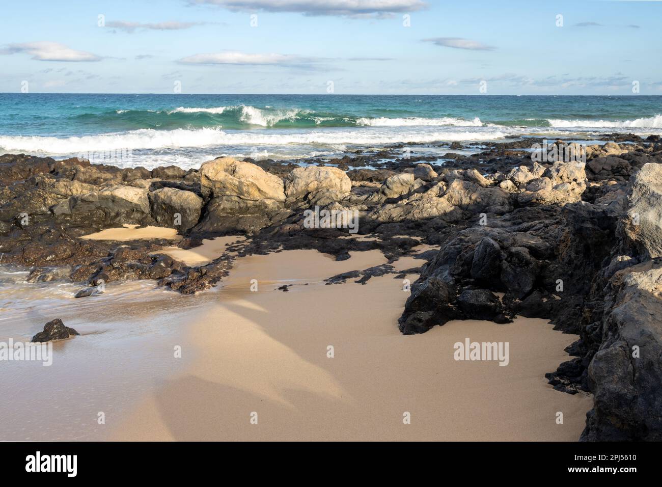Combinaison d'un sable et d'une côte rocheuse à la plage de l'océan Atlantique. Ciel bleu avec nuages blancs. Parque Natural Dunas de Corralejo, Fuerteventura, SP Banque D'Images