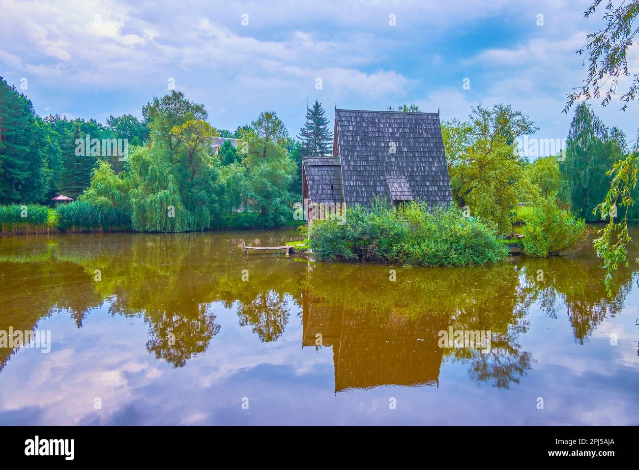 La petite maison de chasseur en bois se reflète sur la surface miroir transparente du lac forestier, situé dans la ferme de chasse de Styr, village de Zbrui, Lviv Banque D'Images