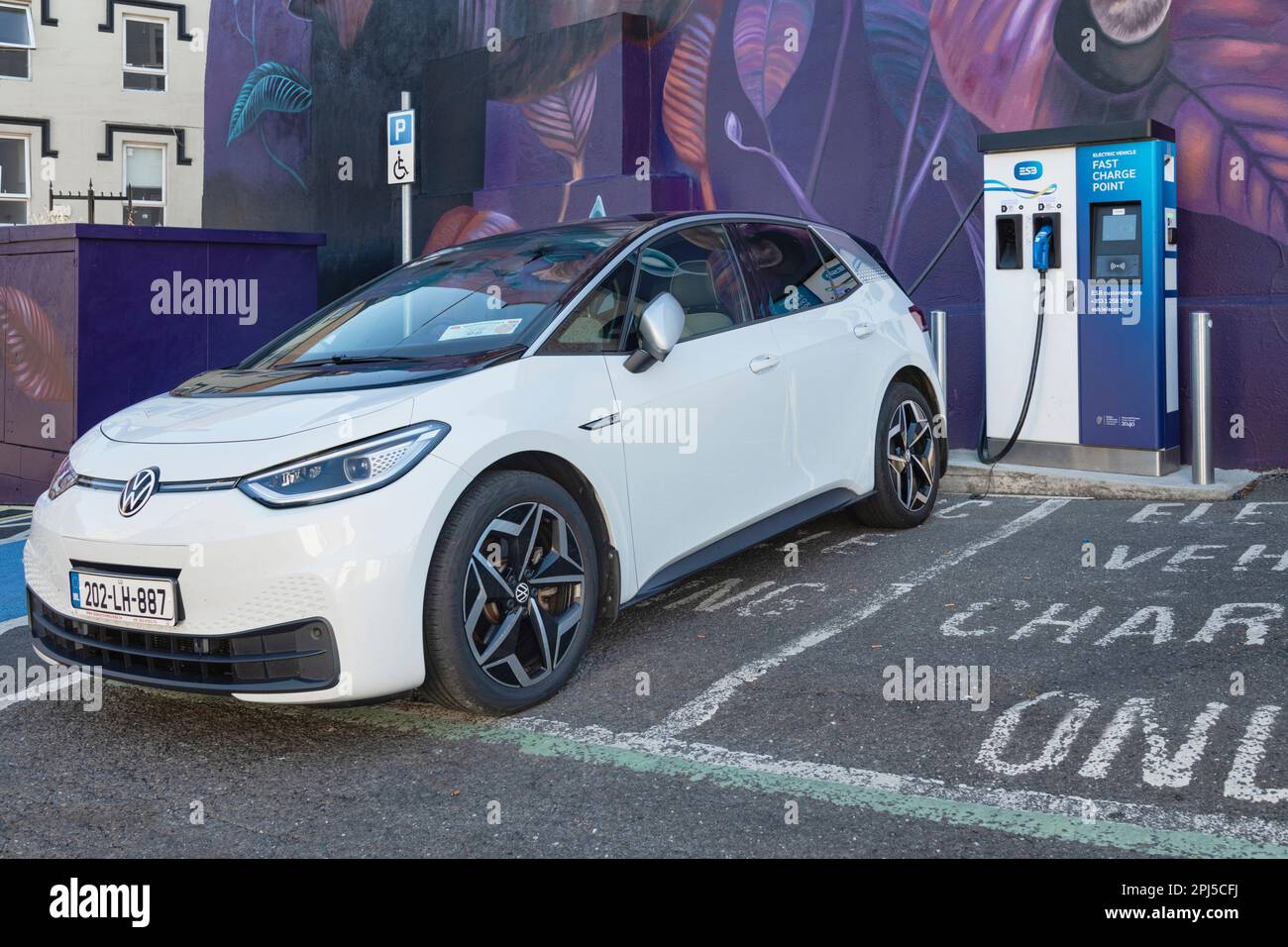 Irlande, Comté de Wexford, New Ross, E-car étant chargé à un point de charge de voiture électrique avec une fresque de l'artiste néerlandais Nina Valkhoff montrant un W normand Banque D'Images