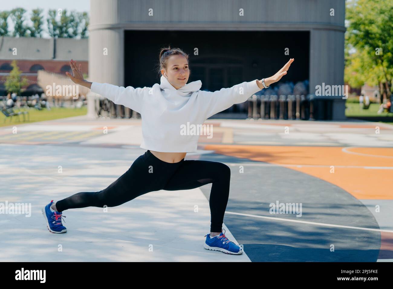 Active jeune femme dédiée à la forme physique fait des exercices d'étirement des mains vêtues en vêtements actifs étire les jambes et les bras poses outdoo. Les gens sont Banque D'Images