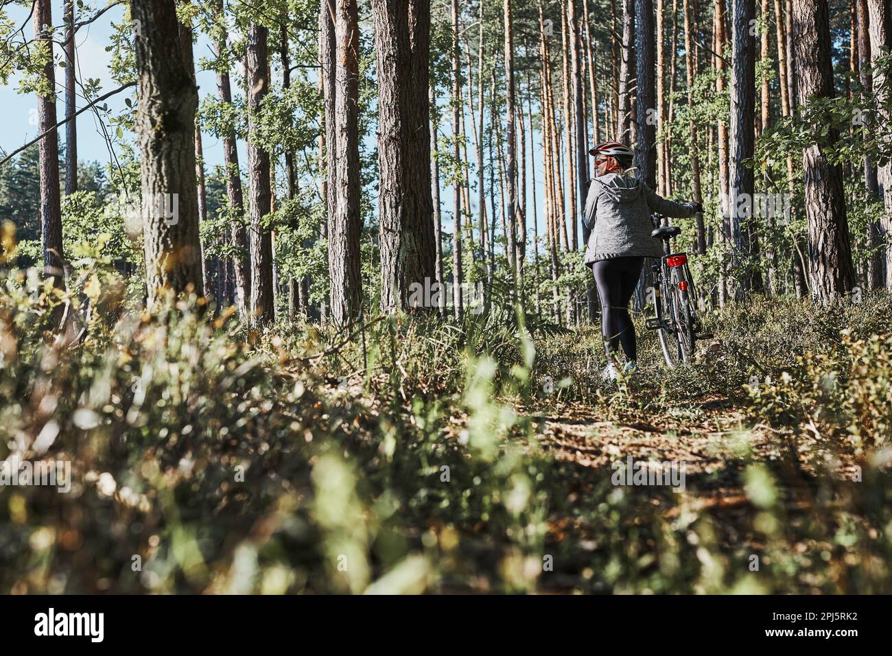 Femme active à vélo sur la route forestière. Une femme qui fait du vélo tout-terrain le jour des vacances d'été. Femme portant un casque de vélo et des gants Banque D'Images