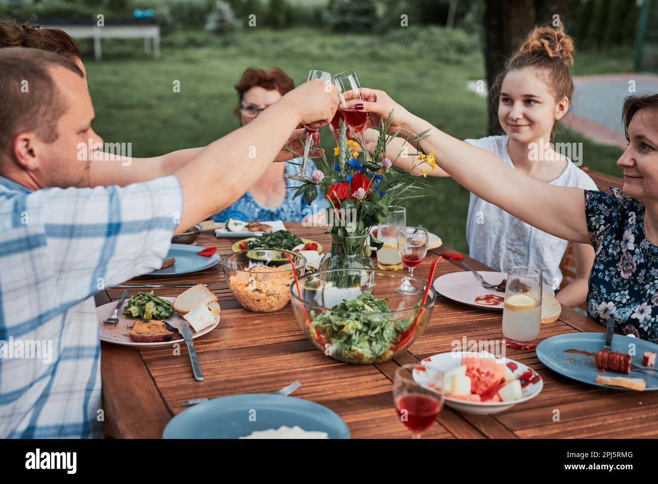 Faites du pain grillé en été pique-nique en plein air dans un jardin à la maison. Gros plan des personnes tenant des verres à vin avec du vin rouge sur la table avec la nourriture A. Banque D'Images