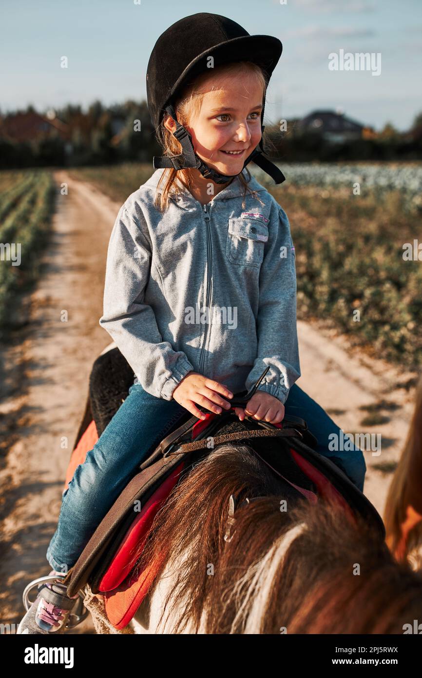 Petite fille souriante apprenant l'équitation. 5-6 ans équestres en casque ayant plaisir à monter un cheval Banque D'Images