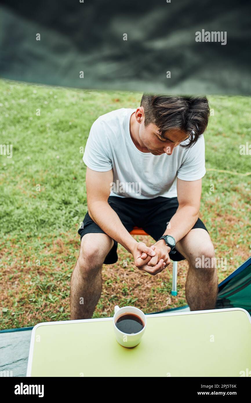 Un jeune homme buvant un café assis devant la tente le matin. Adolescent profitant de temps libre pendant le week-end de voyage en été Banque D'Images