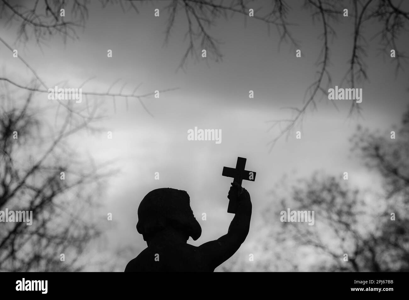 Silhouette d'une statue d'ange, illuminée contre un ciel nocturne, avec une croix à sa portée Banque D'Images