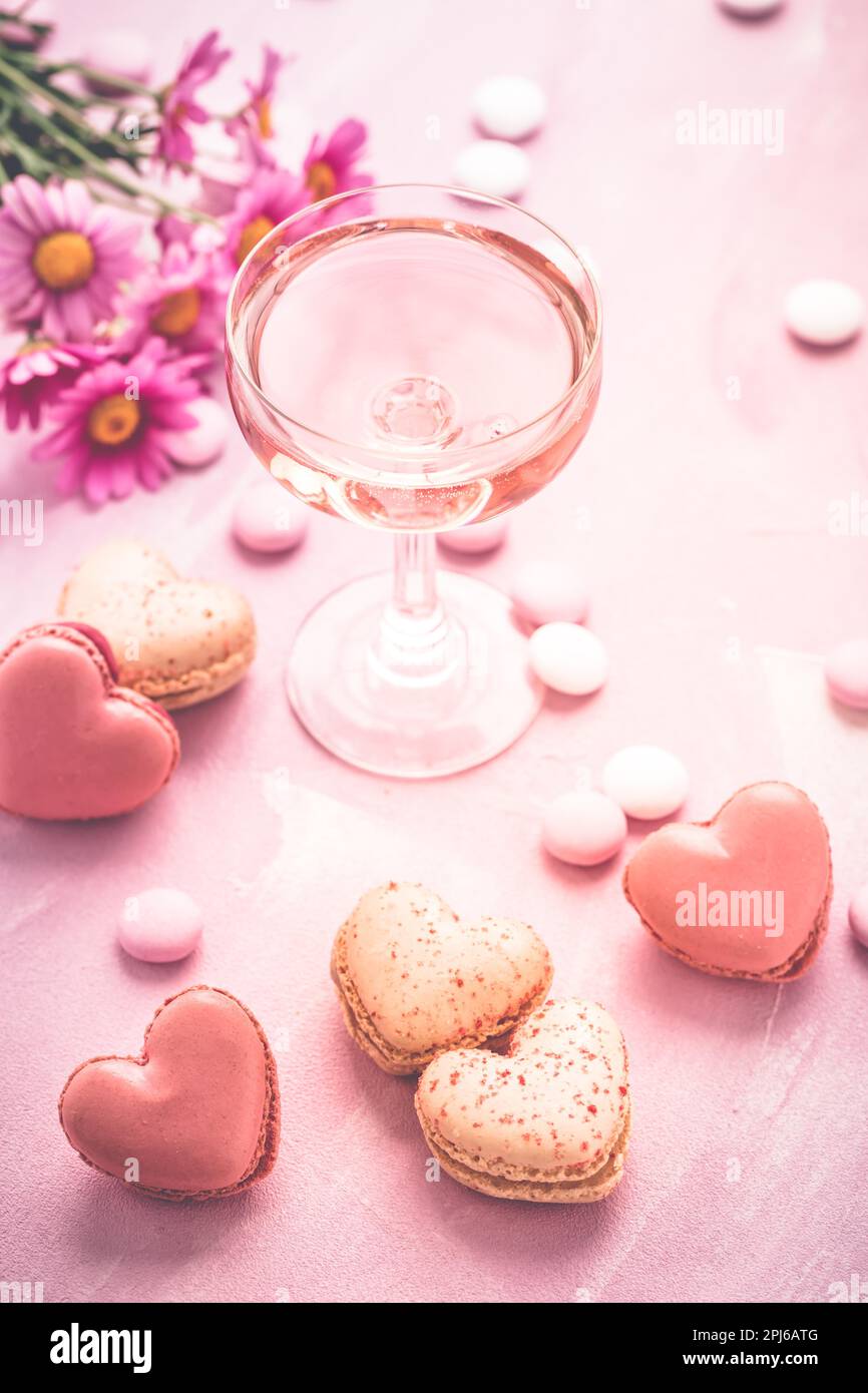 Happy Mothers Day - macarons doux en forme de coeur et verre de vin mousseux rose avec fleurs de tons roses Banque D'Images