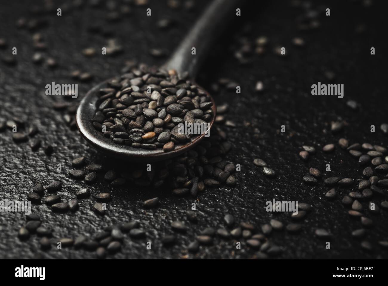 Graines de sésame noir dans une petite cuillère sur fond noir. Prise de vue en studio macro Banque D'Images