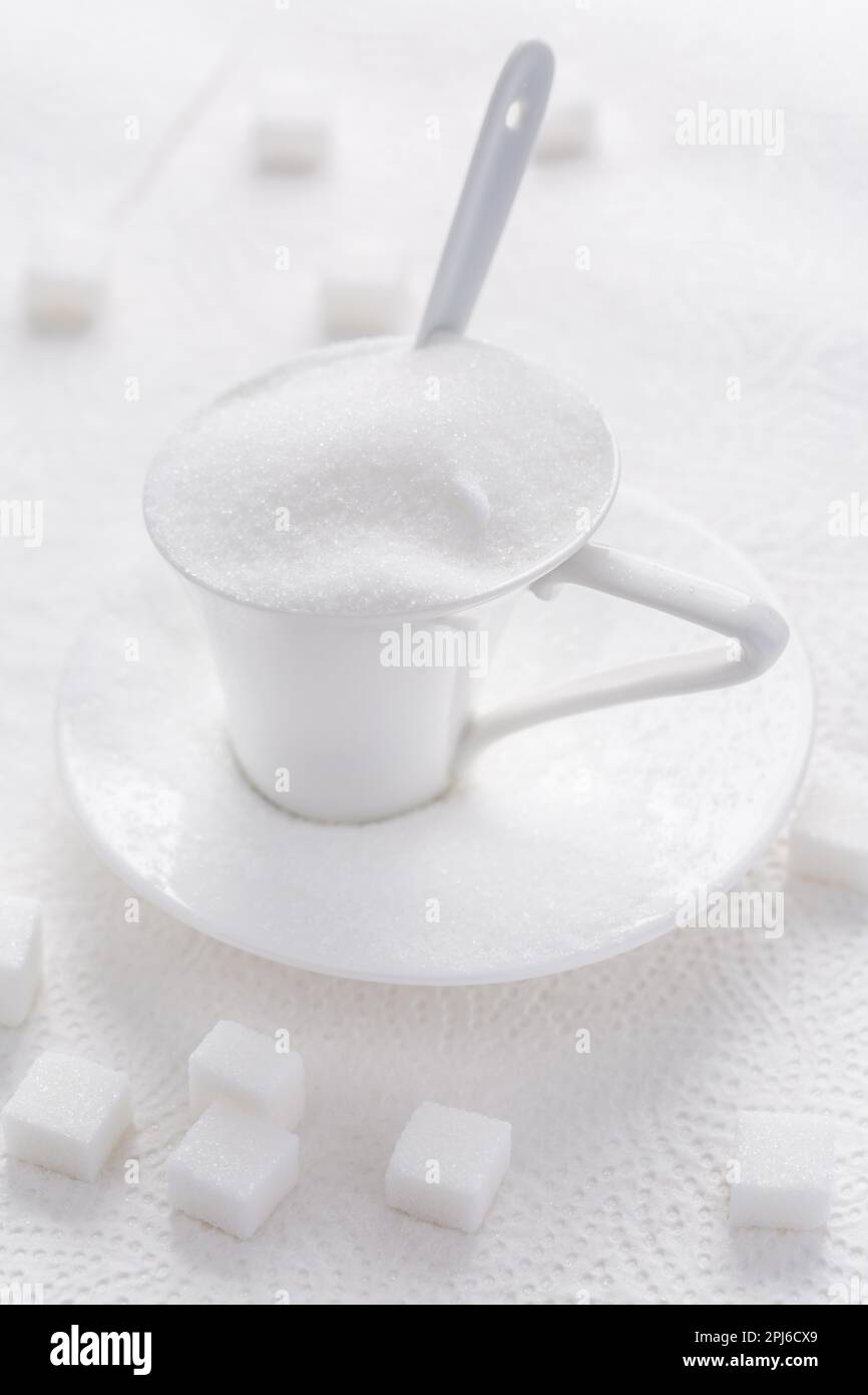 Sucre blanc granulé dans une tasse blanche avec cuillère sur fond blanc Banque D'Images