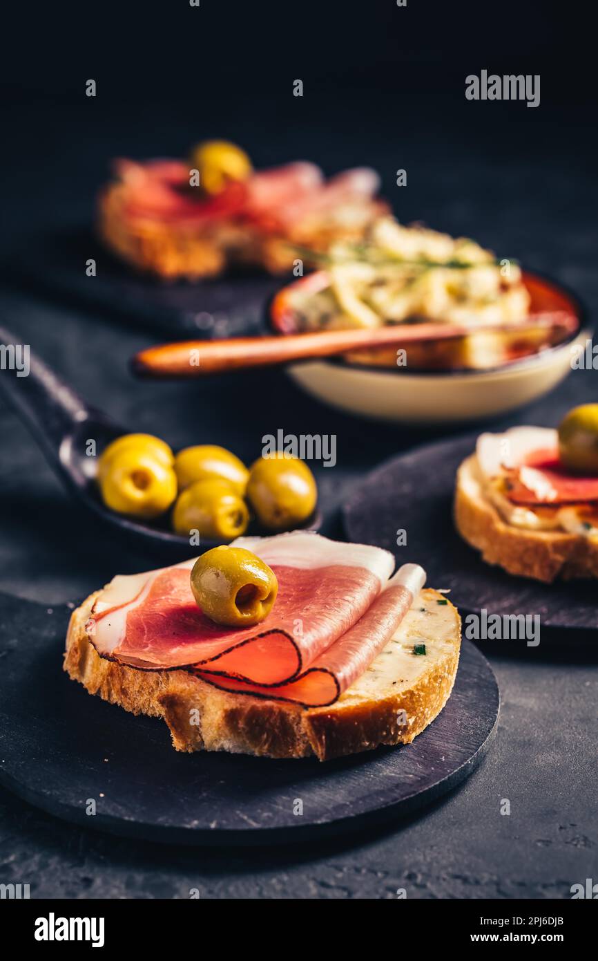 Pain grillé ou sandwich ouvert avec tartiner au beurre d'ail et jambon de serano et olive sur fond sombre Banque D'Images
