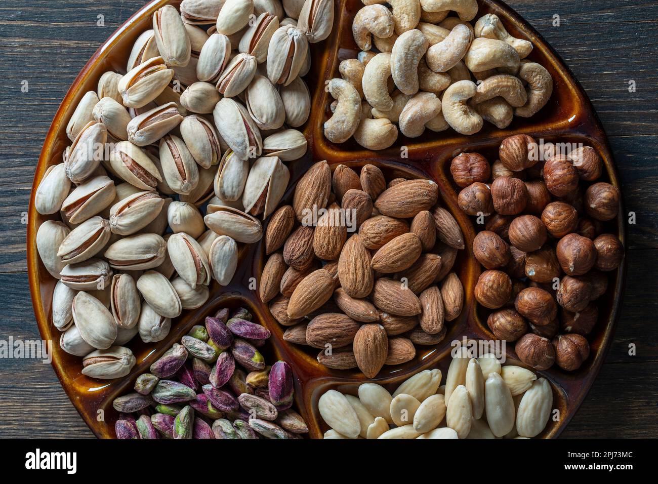 Assortiment de noix dans un bol en céramique sur fond en bois, gros plan, vue de dessus, espace de copie. Noix de cajou, noisettes, pistaches et amandes à manger. Vég Banque D'Images